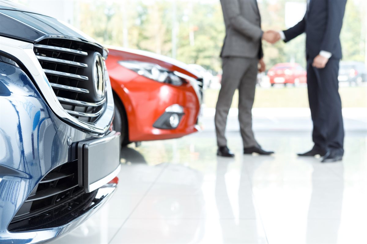 Business partners shaking hands beside new vehicles